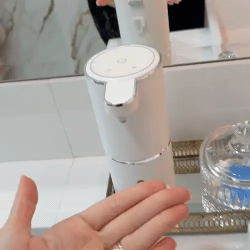 Saboneteira LuxSense sendo acionada sem toque, liberando sabonete na mão em um banheiro elegante